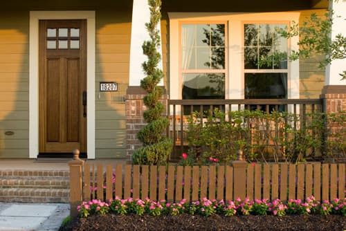 beige house with wood door small wood fence pink flowers